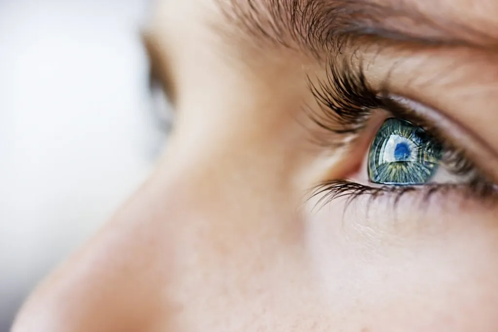 Un primer plano del ojo azul de una mujer mirando hacia el cielo, con las pestañas curvadas
