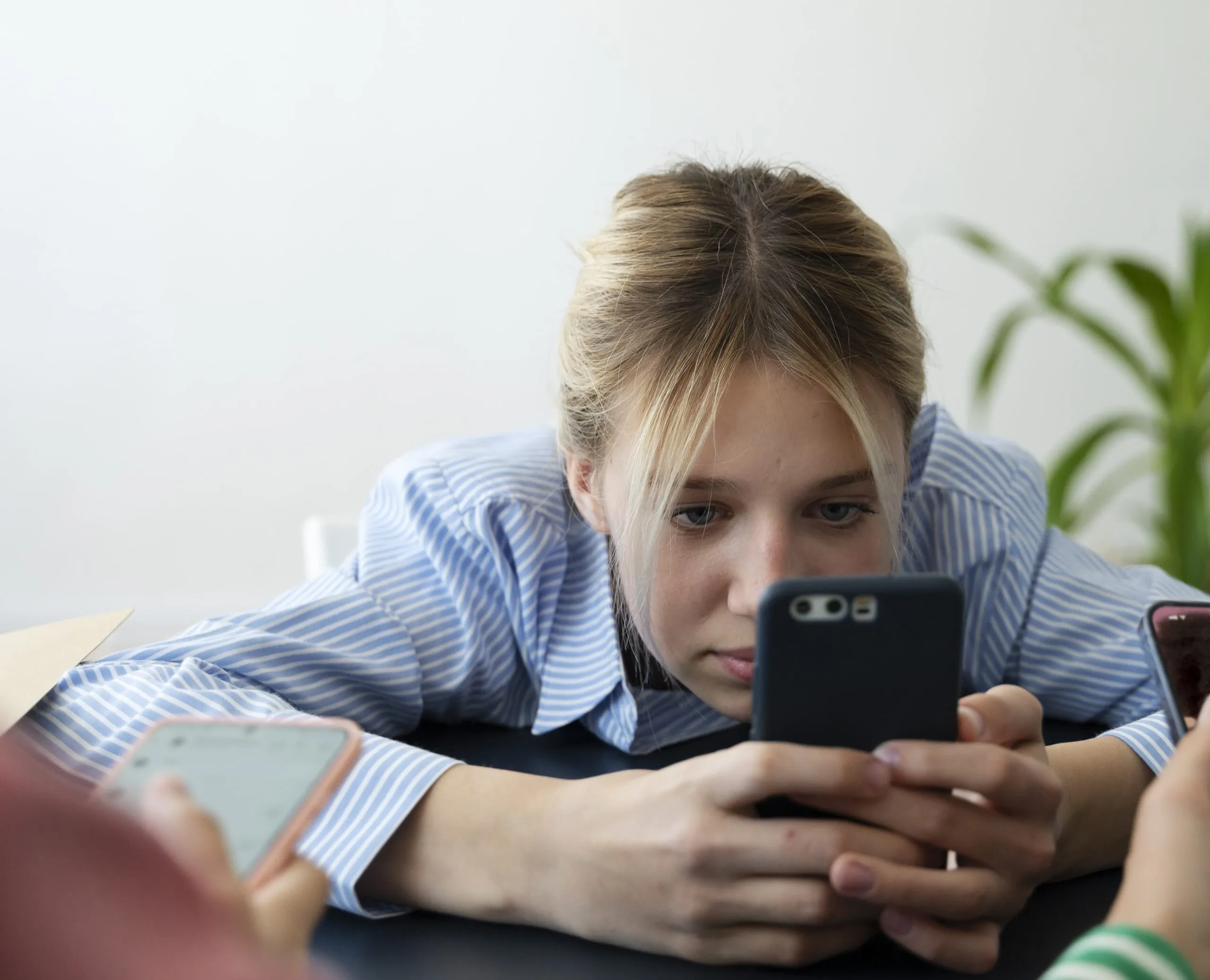 Joven mirando su teléfono móvil mientras se apoya en la mesa, lo que podría reflejar el comportamiento de esfuerzo visual frecuente asociado al espasmo acomodativo